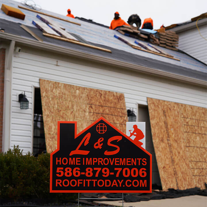 L&S Home Improvements yard sign in front of house that L&S workers in bright orange are working on the roof