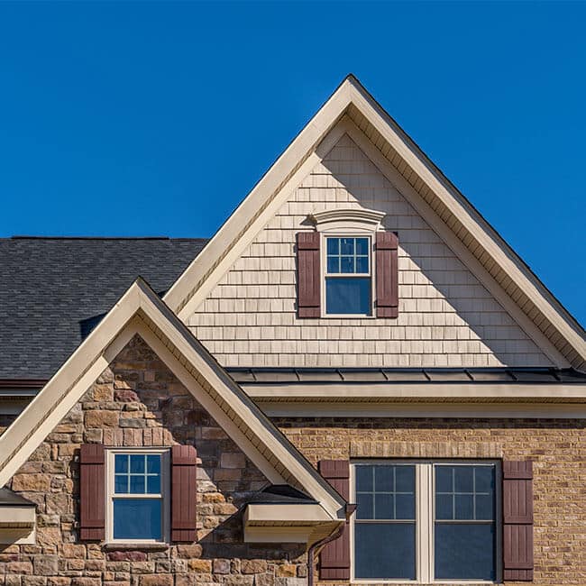 Double triangle gable with double hung sash window with complementing shutters, decorative arched trim, shake and shingle and architectural stone siding, brown eaves through system, fascia, soffit