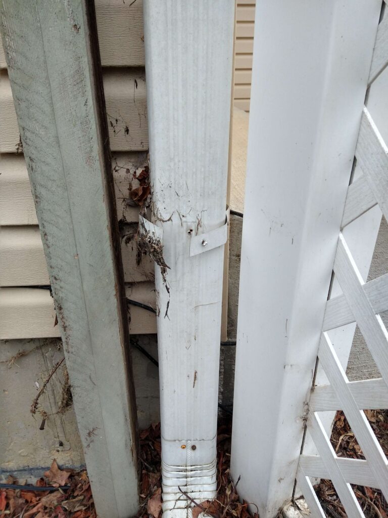 The joint/bracket of one section of a gutter system has popped out, showing an empty hole where the screw used to be that connected the joints together.