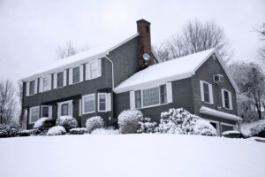 A traditional American colonial home in a snowy winter landscape. There is snow on the roof.