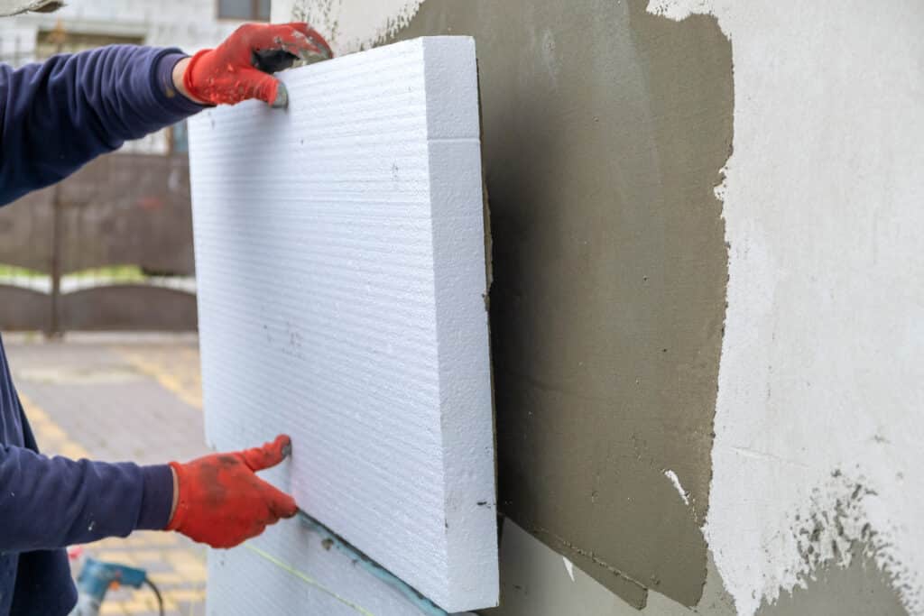 A person installs a styrofoam insulation board on an exterior wall