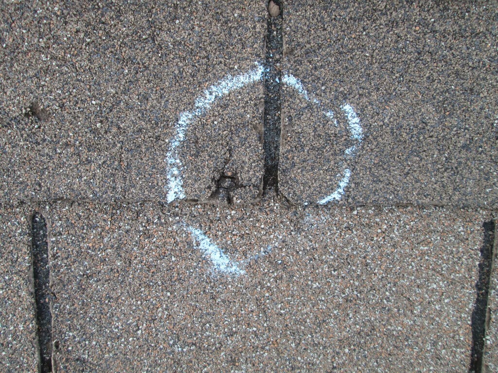 A chalk circle showing a puncture in an asphalt roof shingle